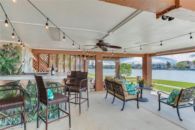 view of patio / terrace featuring ceiling fan, a water view, and exterior bar