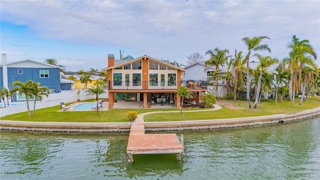 back of house with a pool side deck with water view, a patio area, and a lawn