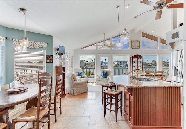 kitchen featuring sink, stainless steel refrigerator with ice dispenser, beamed ceiling, decorative light fixtures, and a kitchen island with sink