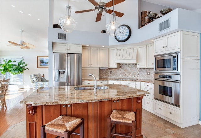 kitchen with white cabinetry, sink, light stone counters, custom range hood, and appliances with stainless steel finishes