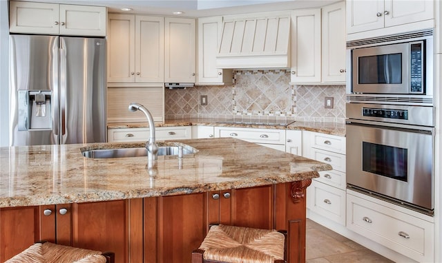 kitchen with sink, light stone counters, premium range hood, white cabinetry, and stainless steel appliances