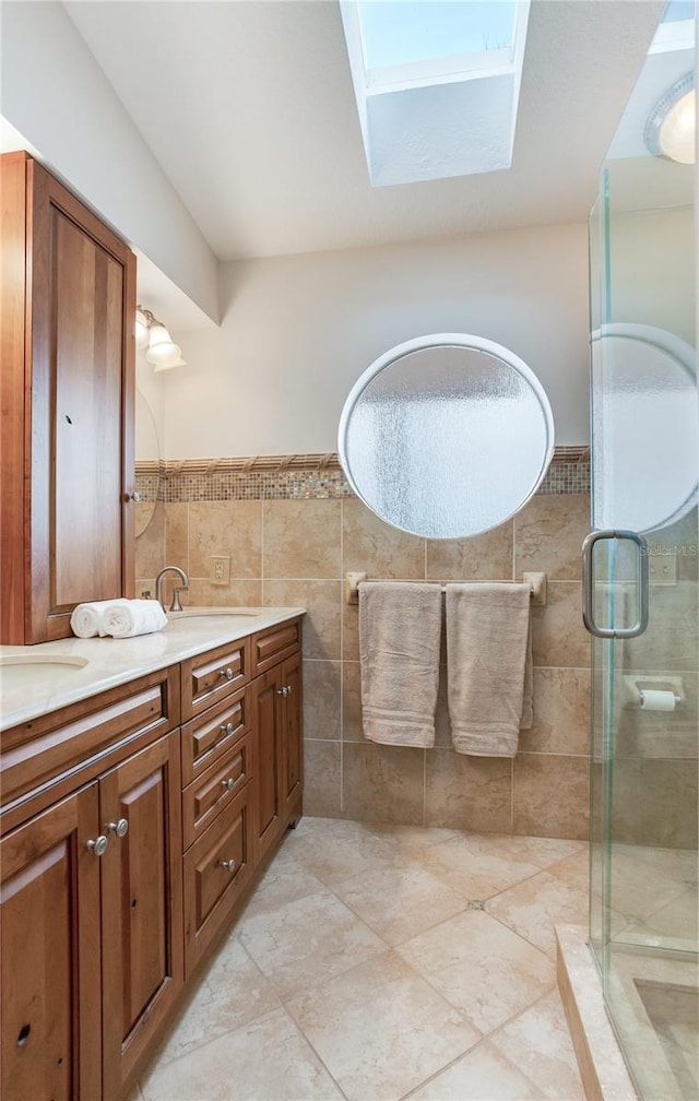 bathroom with tile walls, vanity, a skylight, and a shower with shower door