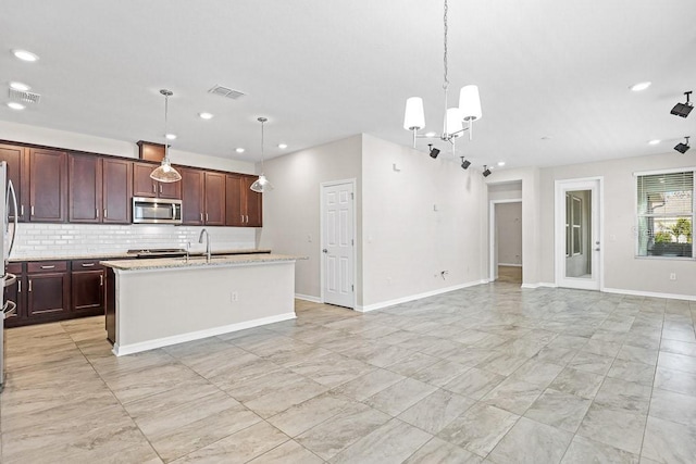 kitchen featuring a kitchen island with sink, a notable chandelier, light stone counters, decorative light fixtures, and backsplash