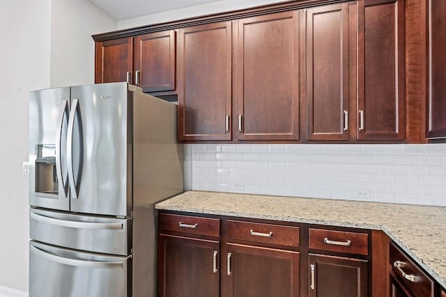 kitchen with decorative backsplash, light stone counters, and stainless steel fridge