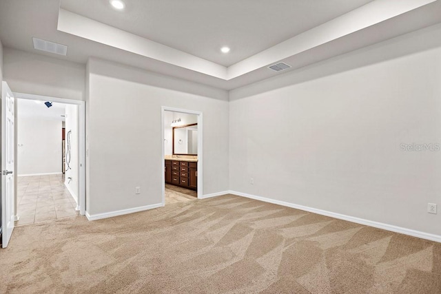 unfurnished bedroom with ensuite bathroom, light colored carpet, and a raised ceiling