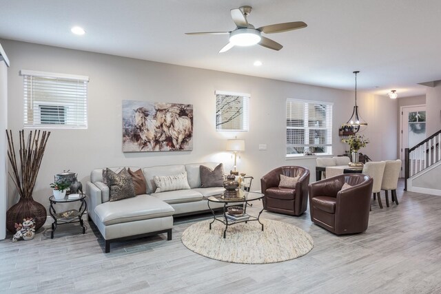 living room featuring ceiling fan with notable chandelier and light hardwood / wood-style flooring