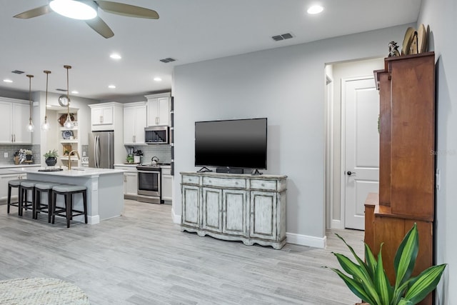 kitchen featuring appliances with stainless steel finishes, hanging light fixtures, an island with sink, white cabinets, and tasteful backsplash