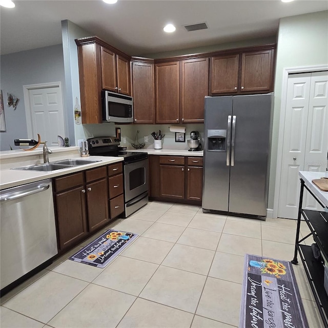 kitchen with sink, dark brown cabinetry, light tile patterned floors, and appliances with stainless steel finishes