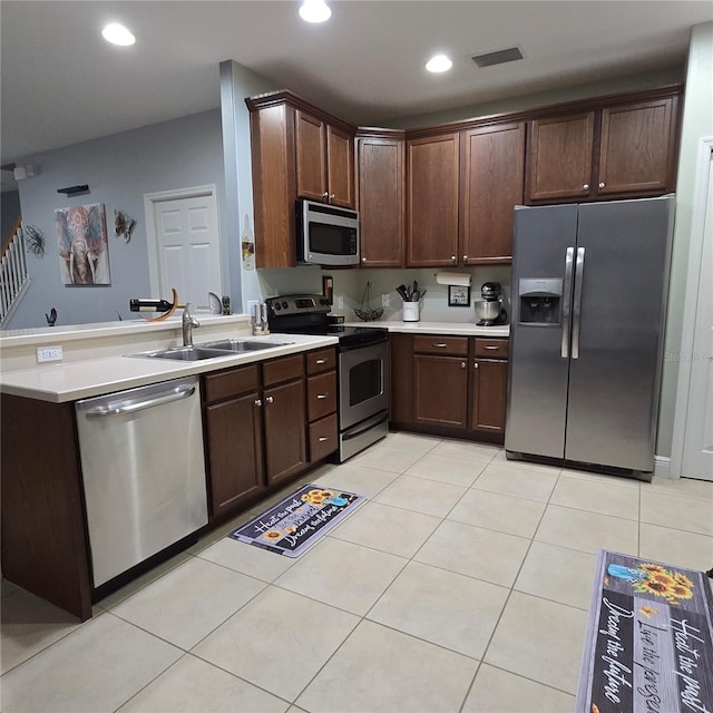 kitchen with appliances with stainless steel finishes, kitchen peninsula, light tile patterned floors, dark brown cabinetry, and sink