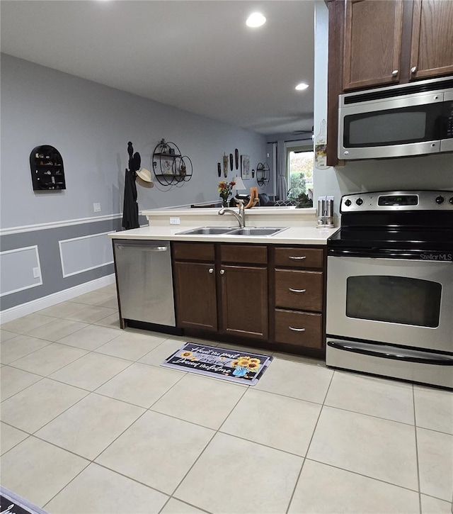 kitchen with sink, light tile patterned floors, kitchen peninsula, dark brown cabinetry, and appliances with stainless steel finishes