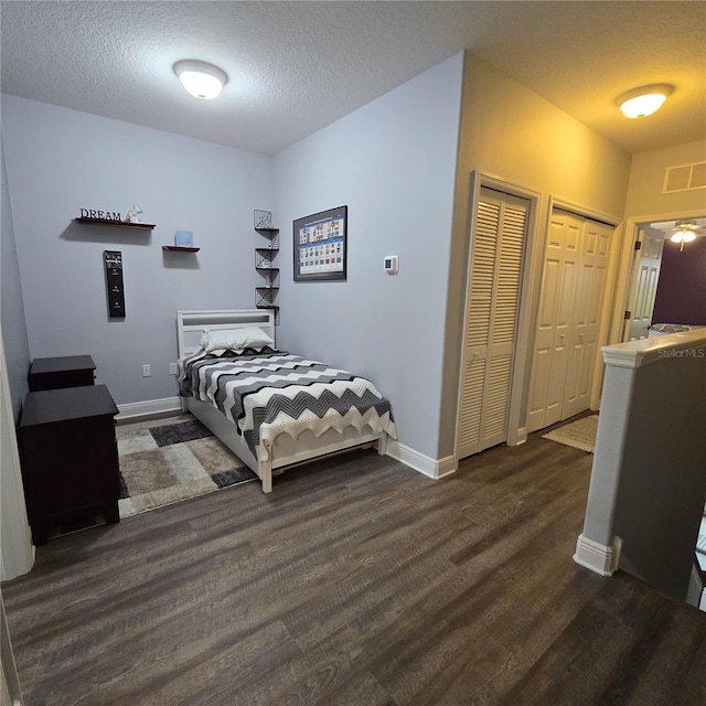 bedroom featuring a textured ceiling, two closets, and dark hardwood / wood-style flooring