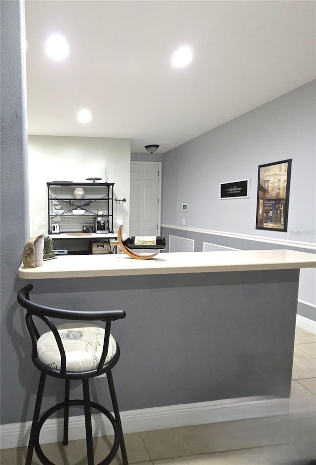 kitchen with lofted ceiling, light tile patterned floors, kitchen peninsula, and a breakfast bar