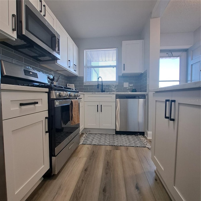 kitchen featuring light hardwood / wood-style flooring, backsplash, white cabinetry, appliances with stainless steel finishes, and sink