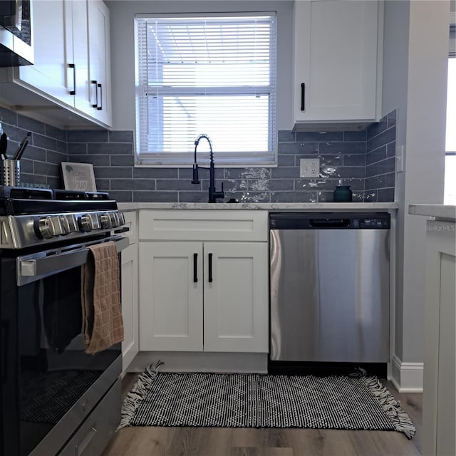 kitchen featuring stainless steel appliances, sink, white cabinets, backsplash, and light stone countertops