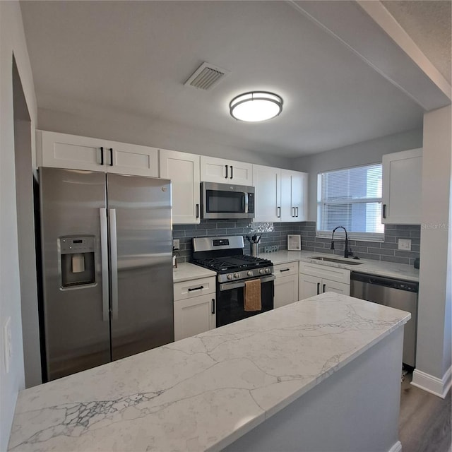 kitchen featuring stainless steel appliances, sink, white cabinets, backsplash, and light stone countertops