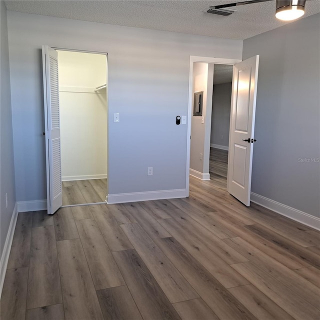 unfurnished bedroom featuring a walk in closet, a textured ceiling, a closet, and hardwood / wood-style floors