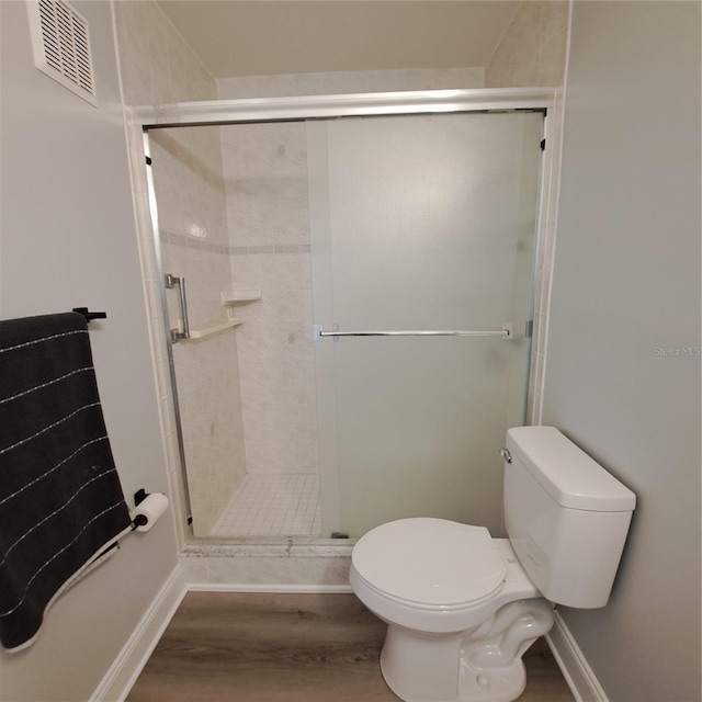 bathroom featuring hardwood / wood-style floors, a shower with shower door, and toilet