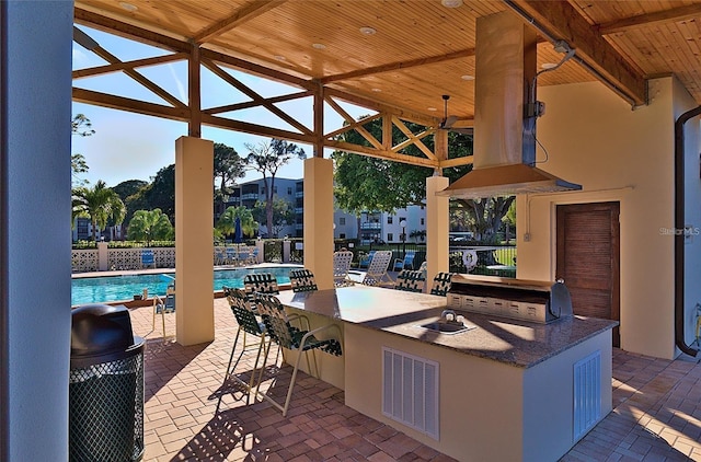 view of patio featuring an outdoor bar, an outdoor kitchen, a community pool, ceiling fan, and a grill