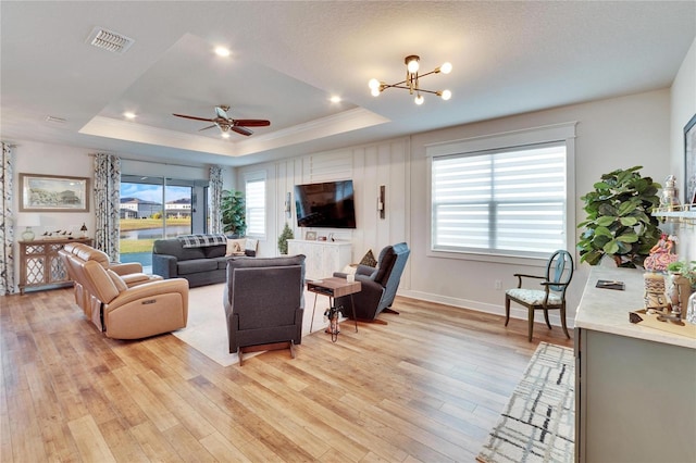 living room with ceiling fan with notable chandelier, light hardwood / wood-style floors, and a tray ceiling