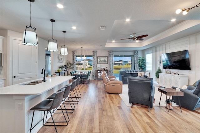 living room featuring sink, ceiling fan, ornamental molding, light wood-type flooring, and a tray ceiling