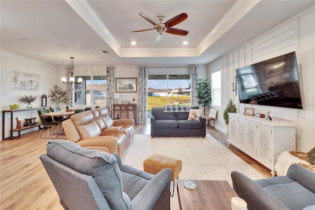 living room with a tray ceiling, crown molding, ceiling fan with notable chandelier, and light wood-type flooring