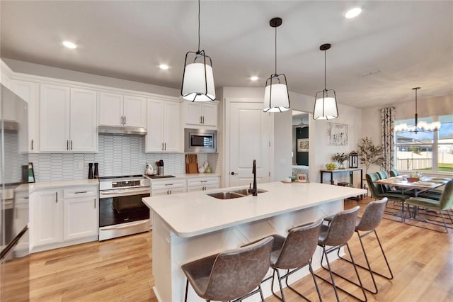 kitchen with white cabinets, stainless steel appliances, a center island with sink, and sink