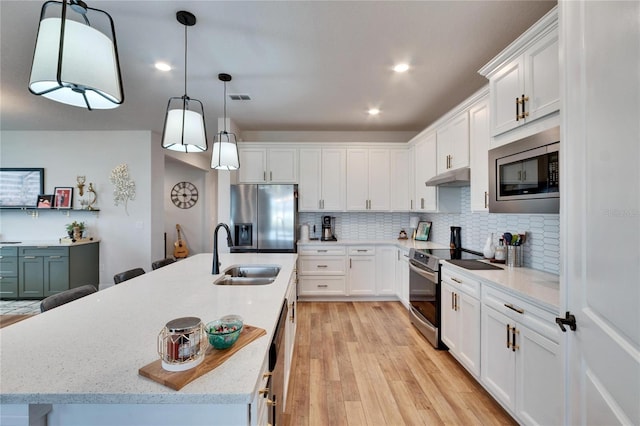 kitchen featuring appliances with stainless steel finishes, a kitchen island with sink, sink, decorative light fixtures, and white cabinetry