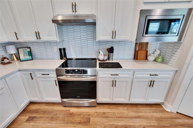 kitchen with white cabinets, decorative backsplash, appliances with stainless steel finishes, and light hardwood / wood-style flooring