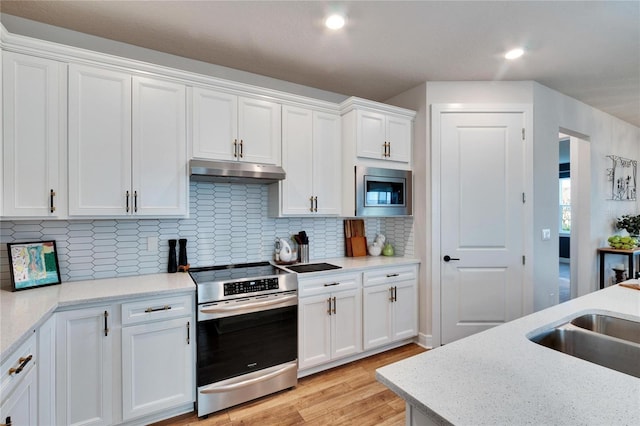 kitchen featuring white cabinets, light hardwood / wood-style flooring, appliances with stainless steel finishes, tasteful backsplash, and light stone counters