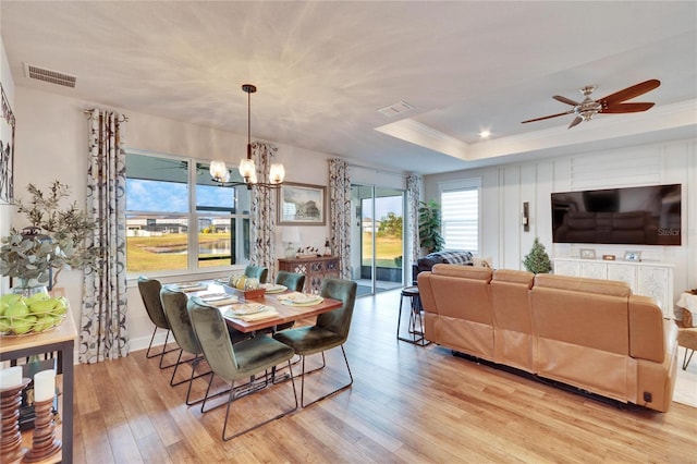 dining area with a tray ceiling, crown molding, light hardwood / wood-style floors, and ceiling fan with notable chandelier