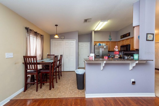 kitchen with kitchen peninsula, a kitchen breakfast bar, stainless steel fridge with ice dispenser, light hardwood / wood-style floors, and hanging light fixtures