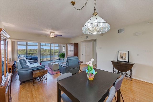 dining area featuring a textured ceiling, ceiling fan with notable chandelier, wood-type flooring, and a water view