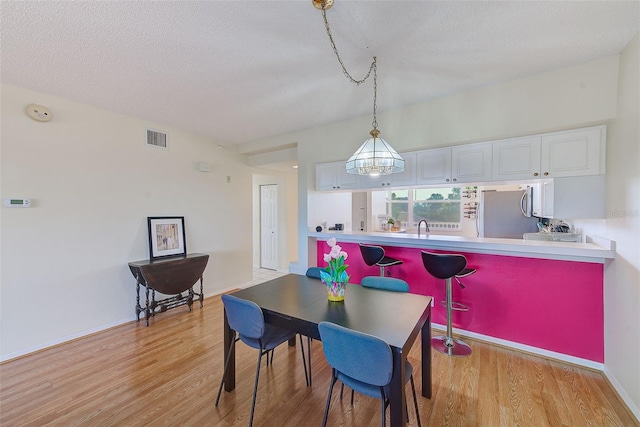 dining space with light hardwood / wood-style floors, sink, and a textured ceiling