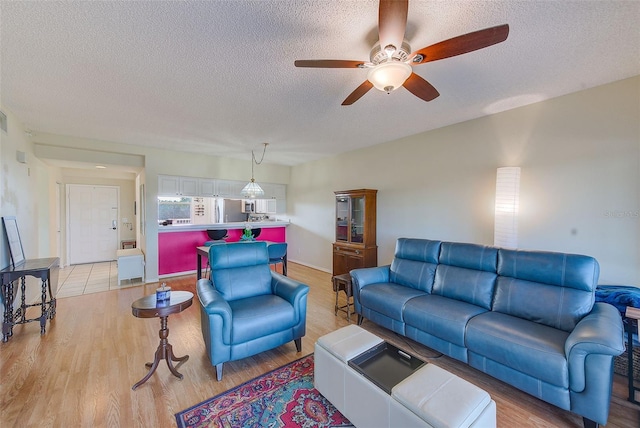 living room with ceiling fan, a textured ceiling, and light wood-type flooring