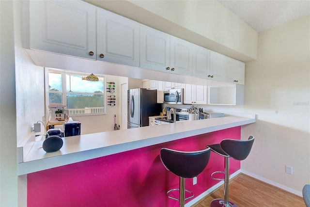 kitchen featuring a kitchen bar, light hardwood / wood-style floors, white cabinetry, and appliances with stainless steel finishes