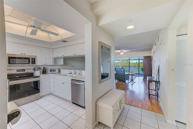 kitchen with ceiling fan, sink, light tile patterned flooring, appliances with stainless steel finishes, and white cabinets