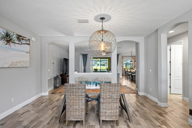 unfurnished dining area featuring a chandelier, a textured ceiling, and light hardwood / wood-style floors