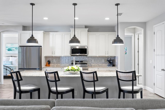 kitchen with a kitchen island with sink, light stone countertops, white cabinets, and appliances with stainless steel finishes