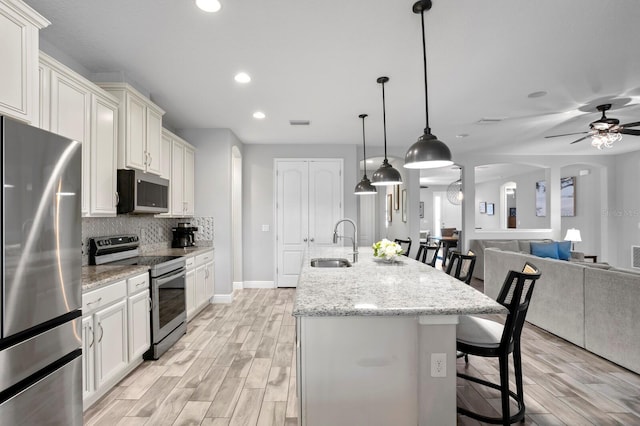 kitchen featuring pendant lighting, sink, stainless steel appliances, an island with sink, and a kitchen bar