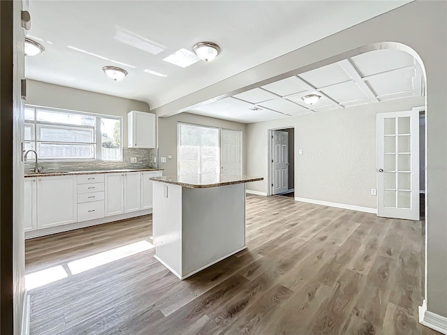 kitchen featuring sink, backsplash, dark stone counters, light hardwood / wood-style floors, and white cabinets