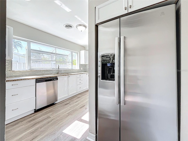 kitchen with backsplash, white cabinets, sink, light wood-type flooring, and stainless steel appliances