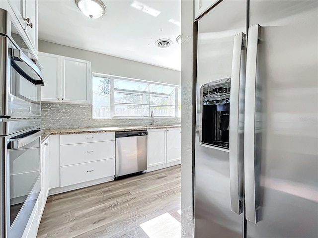 kitchen with white cabinets, decorative backsplash, light wood-type flooring, light stone counters, and stainless steel appliances