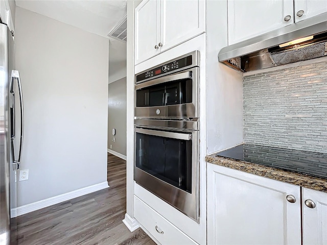 kitchen featuring backsplash, dark stone counters, appliances with stainless steel finishes, range hood, and white cabinetry