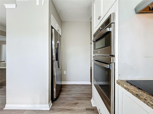 kitchen with white cabinets, light wood-type flooring, stainless steel appliances, and dark stone counters