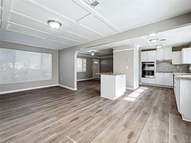 kitchen with backsplash, white cabinets, ceiling fan, light hardwood / wood-style floors, and stainless steel double oven