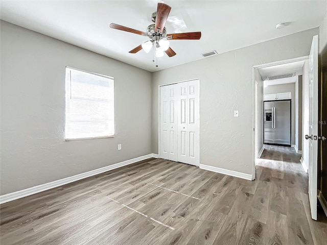 unfurnished bedroom featuring stainless steel fridge with ice dispenser, a closet, ceiling fan, and hardwood / wood-style flooring