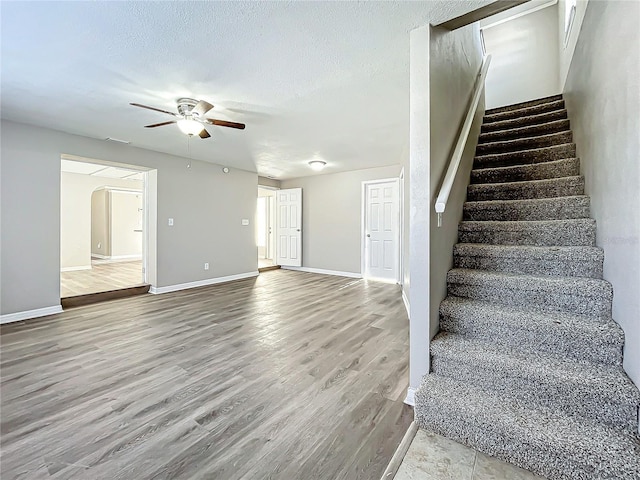 stairway featuring ceiling fan, wood-type flooring, and a textured ceiling