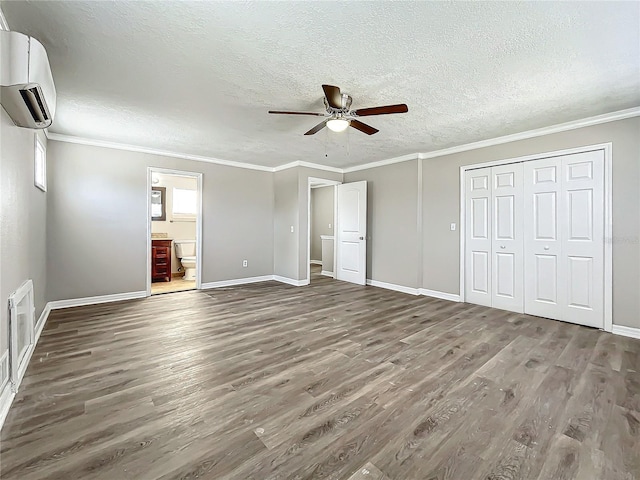 unfurnished bedroom with ensuite bath, ceiling fan, dark wood-type flooring, an AC wall unit, and ornamental molding