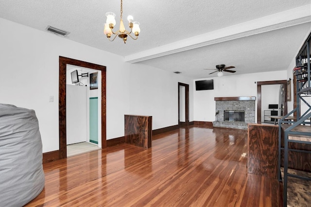 living room featuring ceiling fan with notable chandelier, a brick fireplace, a textured ceiling, beamed ceiling, and wood-type flooring