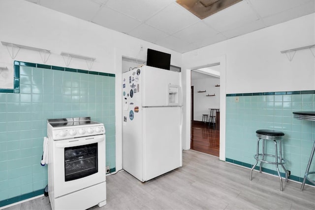 kitchen with a paneled ceiling, light hardwood / wood-style floors, white appliances, and tile walls